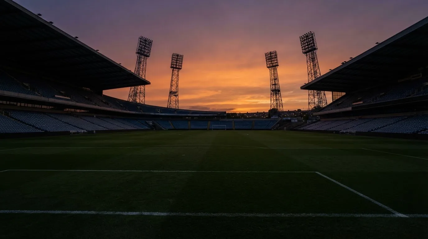 Un estadio de fútbol vacío con torres de iluminación al atardecer